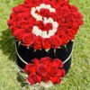 Adana yuvarlak kutuda harfli kırmızı güller, beyaz güllerle harf yazılı ve kutu önü süslemeli çiçek.