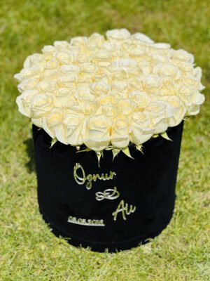 Adana isimli kutuda çiçek, üzerine isim ve tarih yazılı beyaz gül dolu yuvarlak kutu.