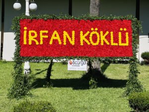 Adana dev gül panosu, kırmızı güllerden çiçek duvarı üzerine beyaz çiçekle isim yazılı lansman dekoru.