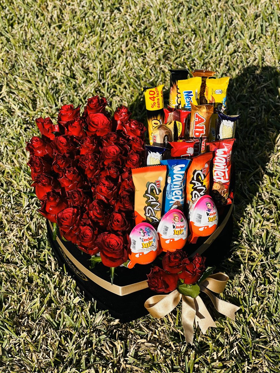 Adana kalp kutuda çiçek ve çikolata, yarısı taze kırmızı güllerle, yarısı çeşitli popüler çikolatalar ve Kinder Joy yumurtalarla dolu siyah lüks kutu.