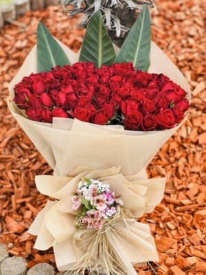 Adana 101 gül kız isteme buketi, doğal kraft kağıda sarılı, egzotik yapraklar ve sap kısmında bahar çiçekleriyle süslenmiş dev kırmızı gül aranjmanı.
