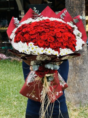 Adana 101 kırmızı gül buketi, dışı beyaz papatyalarla çevrili, vintage çiçek desenli bordo kağıda sarılı, sap kısmında rafya ve mini gül demeti bulunan dev aranjman.