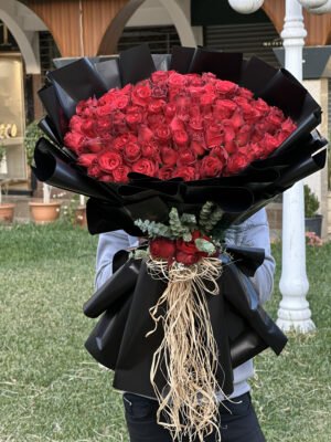 Adana 101 kırmızı gül buketi, lüks mat siyah kağıda sarılı, sap kısmında doğal rafya şelalesi, okaliptüs ve kırmızı gül detayları bulunan dev aranjman.