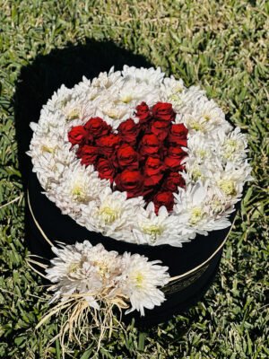 Adana siyah kutuda çiçek, dışı beyaz papatyalarla çevrili ve merkezine kırmızı güllerle kalp motifi işlenmiş romantik yuvarlak kutu aranjmanı.